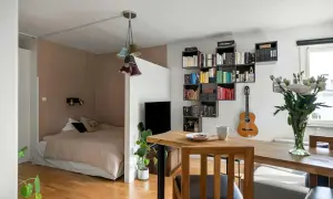 Jak urządzić pokój 4m2? Wygodne łóżko, regały z książkami, gitara i stół z kawą tworzą przytulną przestrzeń.