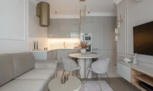 Nowoczesny projekt mieszkania 45m2: salon z beżową kanapą, okrągły stół z krzesłami, kuchnia z szarymi frontami i złoty okap.