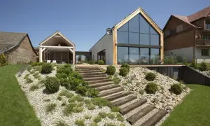 Nowoczesny dom z tarasem i drewnianymi schodami prowadzącymi na skarpę w ogrodzie. Inspiracje dla miłośników zieleni i architektury.