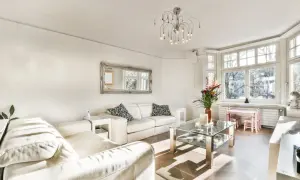 Jasny salon z białymi skórzanymi sofami, szklanym stolikiem i dużym oknem. Elegancki dom w stylu francuskim.