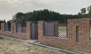 Solidne ogrodzenie z cegły z ozdobnymi metalowymi przęsłami, tworzące elegancką barierę przed lasem.