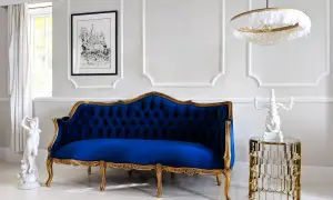 Eleganckie mieszkanie w stylu paryskim: granatowa sofa, złote zdobienia, rzeźba i obraz.