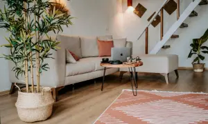 Przytulne, **małe mieszkanie w stylu boho** z beżową kanapą, drewnianym stolikiem i roślinami. Schody prowadzą na piętro.