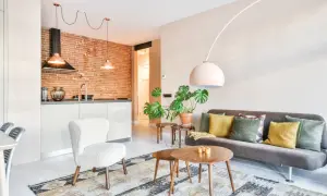 Nowoczesne inspiracje mieszkaniowe: salon z szarą kanapą, biały fotel, stoliki kawowe, rośliny i kuchnia z ceglaną ścianą.