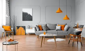 Nowoczesny salon z szarą kanapą, pomarańczowymi akcentami i sztukaterią ścienną inspiracje.