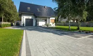 Nowy podjazd do domu z kostki brukowej, prowadzący do garażu. W tle nowoczesny dom i zadbany ogród.