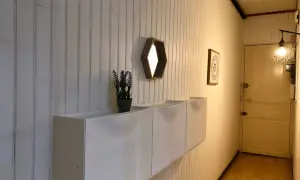 Nowoczesna boazeria w przedpokoju, białe szafki wiszące, lustro i drzwi.