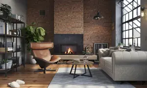 Przytulny, **soft loft** z palącym się kominkiem, skórzanym fotelem i szarą kanapą. Ceglana ściana i drewniana podłoga tworzą ciepłą atmosferę.