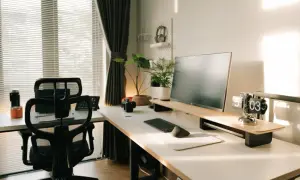 Nowoczesny gabinet w domu z biurkiem, monitorem, klawiaturą, myszką i wygodnym fotelem. Słońce wpada przez okno, tworząc przytulną atmosferę.