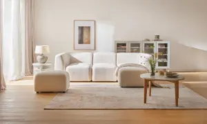 Jasny, przytulny salon z beżową kanapą i pufą. Na podłodze dywan i drewniana podłoga.