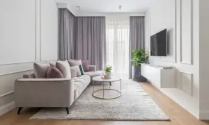 Elegancki salon w stylu modern classic. Jasna kanapa, okrągły stolik kawowy, dywan i zasłony tworzą przytulną atmosferę.