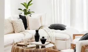 Przytulny salon w stylu boho: biała kanapa z poduszkami, stolik z rattanu, wazon i roślina.