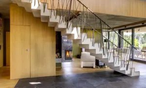 Nowoczesna klatka schodowa w domu z betonu i drewna, z widokiem na kominek i salon.