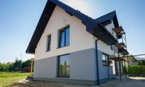 Nowy dom z dwukolorową elewacją, biało-szarą, czeka na malowanie elewacji domu wzory. Rusztowanie ułatwia pracę.