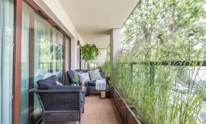 Przytulny balkon w bloku z wygodną sofą i stolikiem, otoczony bujną zielenią traw ozdobnych. Idealne miejsce na relaks.