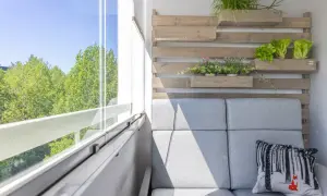 Przytulny mały balkon w bloku z szarą sofą, poduszką z liskiem i zielenią na drewnianej ściance.