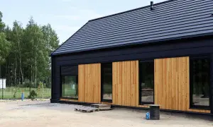 Nowoczesny modulo house z drewnianą elewacją i czarnym dachem, otoczony drzewami.