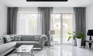 Eleganckie mieszkanie w stylu glamour z szarą, pikowaną kanapą, szklanymi stolikami i błyszczącą podłogą.