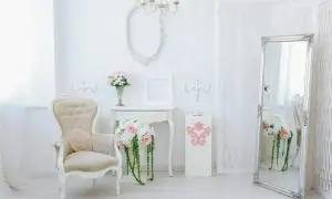 Eleganckie wnętrze w stylu shabby chic: kremowa sofa, lustro w ozdobnej ramie, świeczniki i bukiety kwiatów.