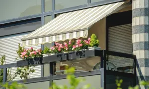 Pasiasty markiza nad balkonem w bloku, z kwitnącymi różowymi kwiatami w skrzynkach, to świetny sposób, jak osłonić balkon.