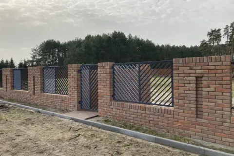Solidne ogrodzenie z cegły z ozdobnymi metalowymi przęsłami, tworzące elegancką barierę przed lasem.