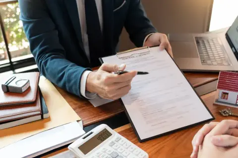 Biznesmen z długopisem wskazuje na umowę kupna. Obok leży model domu, klucz i kalkulator. To pokazuje, co to jest wibor w kontekście kredytu hipotecznego.