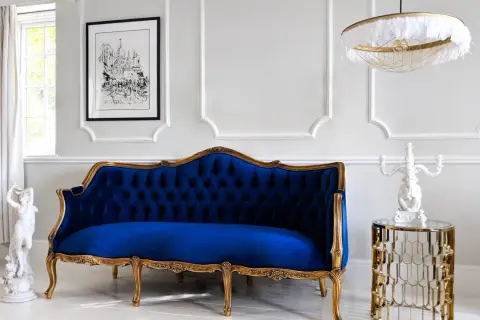 Eleganckie mieszkanie w stylu paryskim: granatowa sofa, złote zdobienia, rzeźba i obraz.