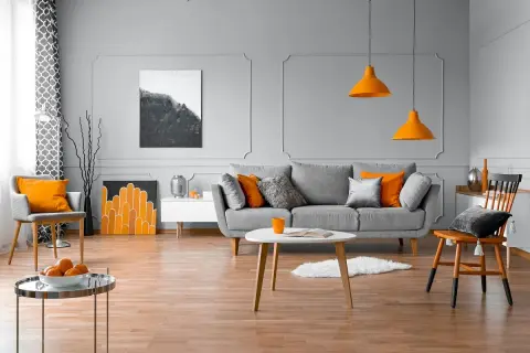 Nowoczesny salon z szarą kanapą, pomarańczowymi akcentami i sztukaterią ścienną inspiracje.