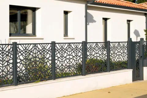 Nowoczesne, ażurowe ogrodzenie z metalu, z geometrycznym wzorem liści, stanowi ozdobę domu. To jedne z najładniejszych ogrodzeń domów.