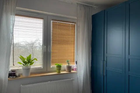Eleganckie żaluzje bambusowe aranżacje okna, tworzące przytulną atmosferę. Obok niebieska szafa.