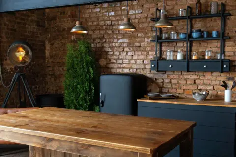 Drewniany stół i ceglana ściana tworzą przytulne loftowe wnętrza inspiracje. Widać lodówkę retro, industrialną lampę i wiszące lampy.