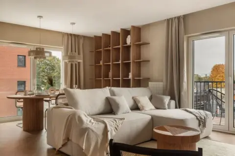 Przytulny salon z beżową kanapą, drewnianym regałem i okrągłym stołem. Piękne wnętrza inspiracje dla Twojego domu.