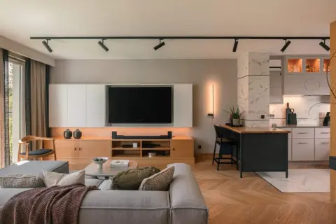 Nowoczesny salon z aneksem kuchennym, gdzie każdy detal tworzy elegancki dom. Drewniana podłoga w jodełkę, szara sofa i wyspa kuchenna.