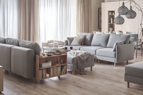Jasne wnętrza inspiracje: przytulny salon z szarą sofą, drewnianymi meblami i zasłonami.