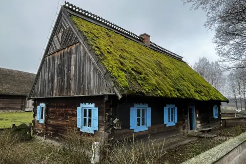 Stylowe domy wiejskie z drewnianymi ścianami i dachami pokrytymi mchem. Jasnoniebieskie okiennice dodają uroku.