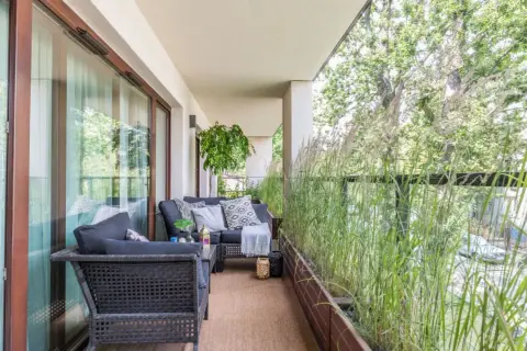 Przytulny balkon w bloku z wygodną sofą i stolikiem, otoczony bujną zielenią traw ozdobnych. Idealne miejsce na relaks.