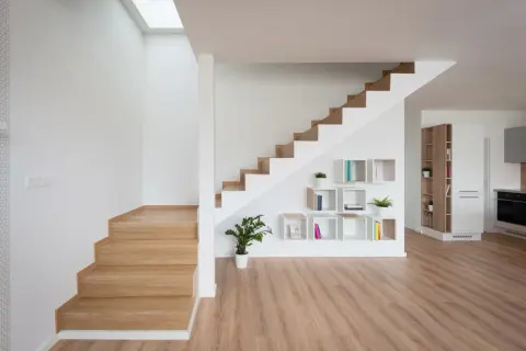 Nowoczesna klatka schodowa inspiracje: drewniane stopnie, białe ściany, geometryczne półki z książkami i roślinami.