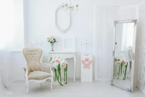 Eleganckie wnętrze w stylu shabby chic: kremowa sofa, lustro w ozdobnej ramie, świeczniki i bukiety kwiatów.