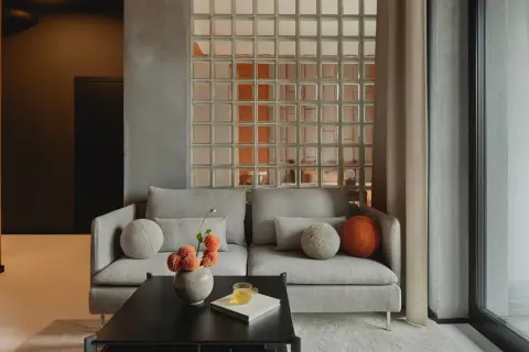 Nowoczesne luksfery aranżacje tworzą subtelny podział w salonie. Szara sofa z ozdobnymi poduszkami i wazonem z kwiatami.