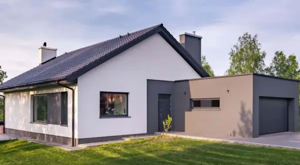 Nowoczesny dom z białymi i grafitowymi ścianami, idealnie wpisujący się w najmodniejsze kolory elewacji. Dachówka i okna w ciemnym odcieniu.