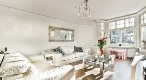 Jasny salon z białymi skórzanymi sofami, szklanym stolikiem i dużym oknem. Elegancki dom w stylu francuskim.