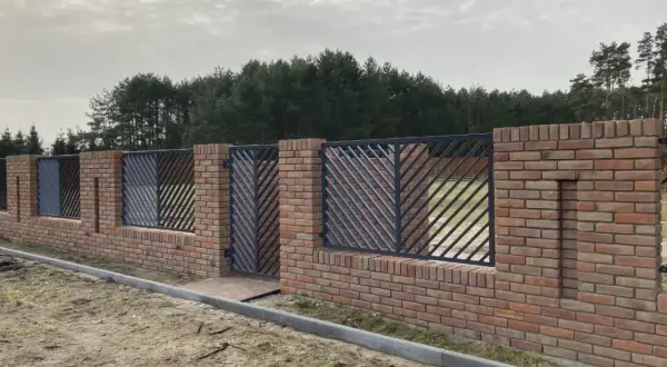 Solidne ogrodzenie z cegły z ozdobnymi metalowymi przęsłami, tworzące elegancką barierę przed lasem.