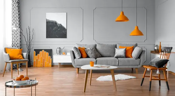 Nowoczesny salon z szarą kanapą, pomarańczowymi akcentami i sztukaterią ścienną inspiracje.