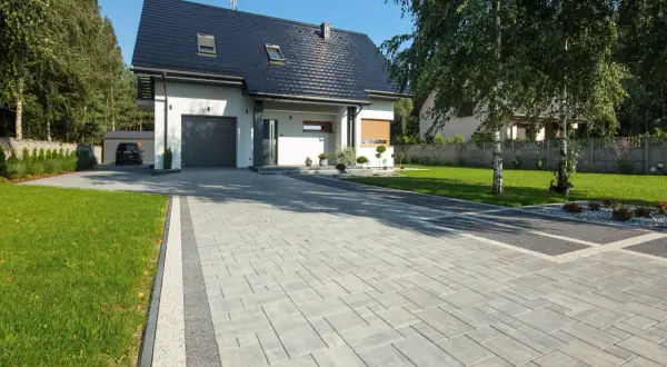 Nowy podjazd do domu z kostki brukowej, prowadzący do garażu. W tle nowoczesny dom i zadbany ogród.