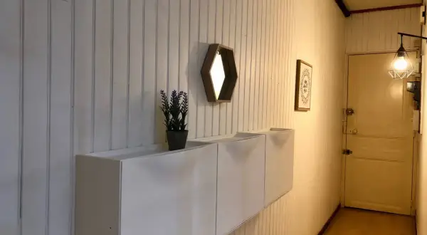 Nowoczesna boazeria w przedpokoju, białe szafki wiszące, lustro i drzwi.
