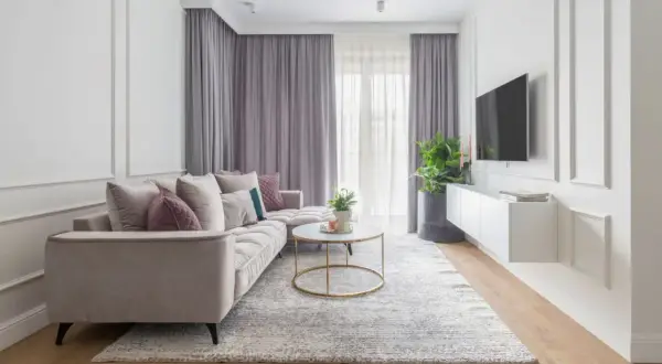 Elegancki salon w stylu modern classic. Jasna kanapa, okrągły stolik kawowy, dywan i zasłony tworzą przytulną atmosferę.