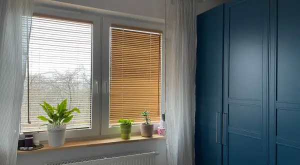 Eleganckie żaluzje bambusowe aranżacje okna, tworzące przytulną atmosferę. Obok niebieska szafa.
