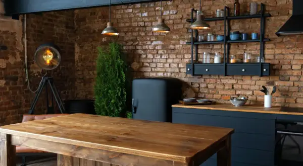 Drewniany stół i ceglana ściana tworzą przytulne loftowe wnętrza inspiracje. Widać lodówkę retro, industrialną lampę i wiszące lampy.