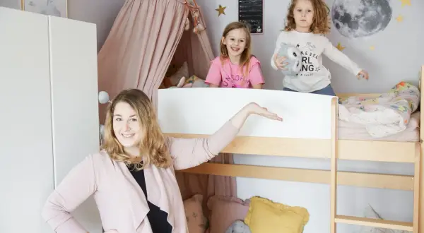 Uroczy mały pokój dla rodzeństwa w bloku. Dwie dziewczynki bawią się na łóżku piętrowym, a mama prezentuje przestrzeń.