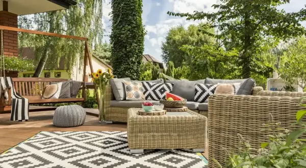 Przytulny taras w stylu boho z wiklinowymi meblami, huśtawką i geometrycznym dywanem. Idealne miejsce na relaks wśród zieleni.